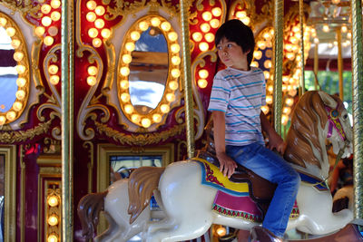 Boy looking away while sitting on carousel horse