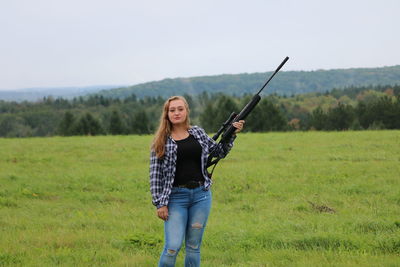 Portrait of teenage girl holding rifle while standing on field