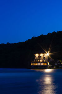 Illuminated buildings by sea against clear blue sky at night