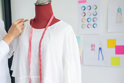 Midsection of fashion designer holding white dress on model at studio
