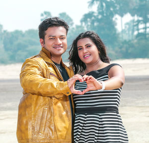 Portrait of couple making heart shape while standing at beach