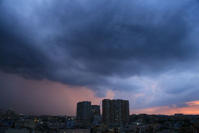 Buildings in city against dramatic sky