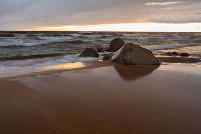 Rocks on beach against sky during sunset