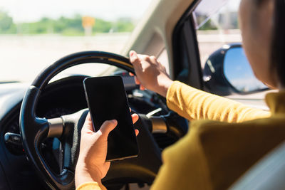 Midsection of woman using smart phone while driving car