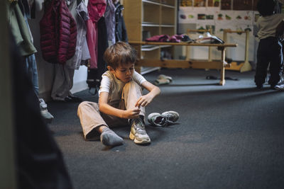 Boy tying shoelace while sitting on floor in cloakroom at preschool