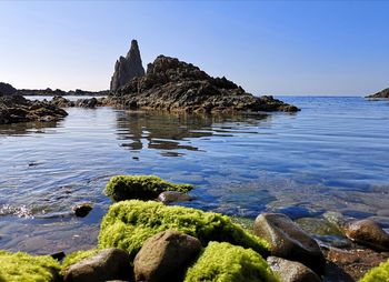 Rocks on sea shore against clear blue sky