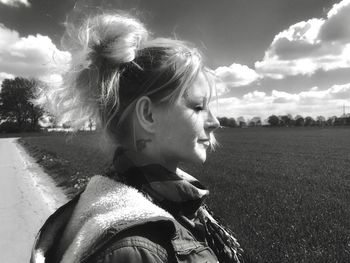 Young woman by car on field against sky