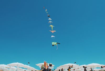 Low angle view of people flying kites against clear blue sky