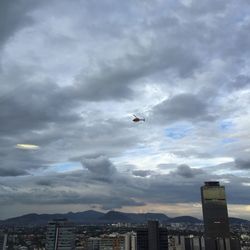 Airplane flying over city against cloudy sky