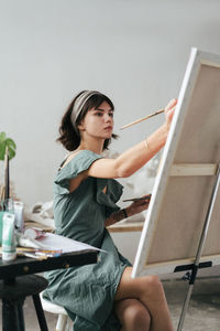 Young woman painting on canvas while sitting on table