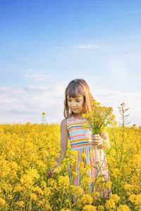Girl plucking yellow flower in field