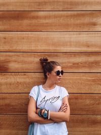 Woman wearing sunglasses standing against wooden wall