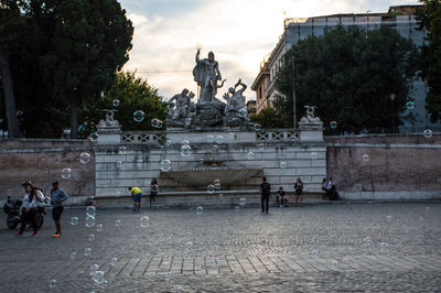 Statue by fountain in city against sky