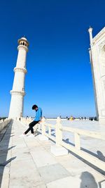 Low angle view of man sitting on a  fence of architecture 