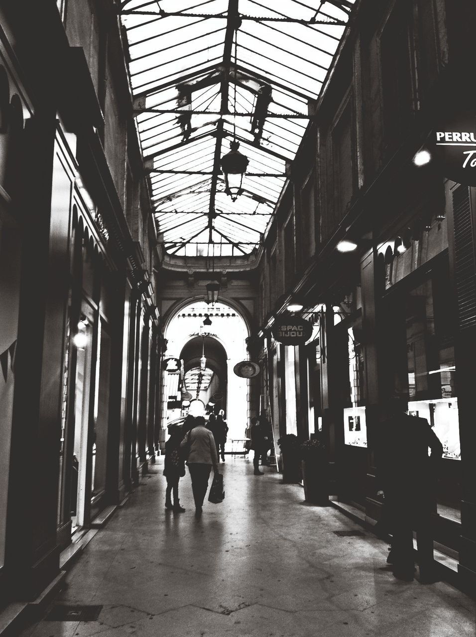 indoors, architecture, built structure, men, walking, corridor, ceiling, person, lifestyles, the way forward, full length, rear view, flooring, illuminated, city life, lighting equipment, tiled floor, leisure activity, building