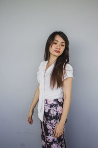 Young woman with eyes closed standing against gray background