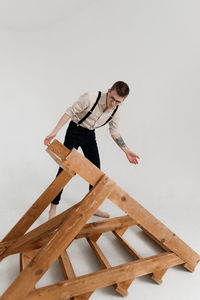 Young man with wooden ladder standing against white background