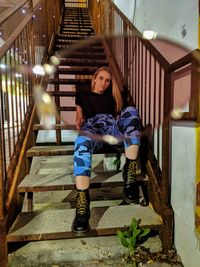 Full length portrait of young woman sitting on staircase of building