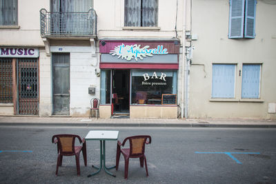 Empty chairs and tables on street against building