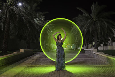 Woman standing by palm tree at night