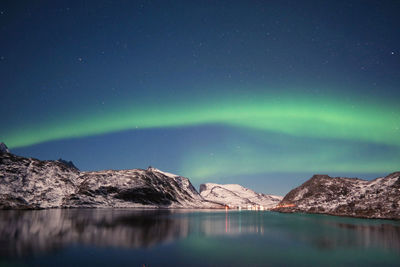 Stunning dancing northern lights over snowy mountains and sea coast in lofoten islands, norway. 