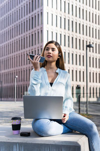Businesswoman talking on phone while sitting against building