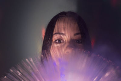 Close-up portrait of young woman holding illuminated fiber optic in darkroom