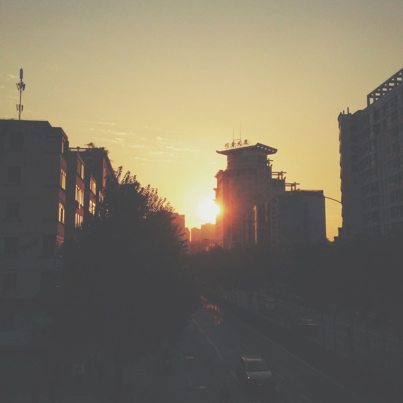 building exterior, architecture, built structure, sunset, city, sun, transportation, silhouette, orange color, clear sky, sky, sunlight, building, car, mode of transport, land vehicle, residential building, street, outdoors, crane - construction machinery