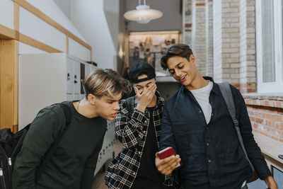 Teenage boy sharing smart phone with friends while walking in school corridor