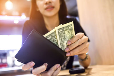 Close-up of woman putting paper currency in wallet at table