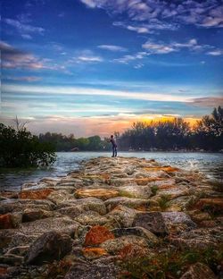 Man standing by lake against sky during sunset