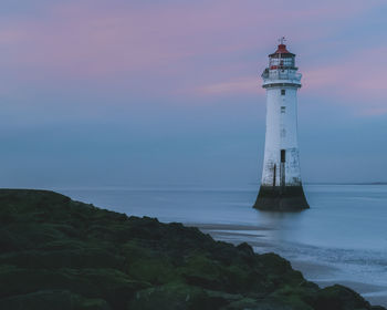 Lighthouse by sea against sky at sunset 