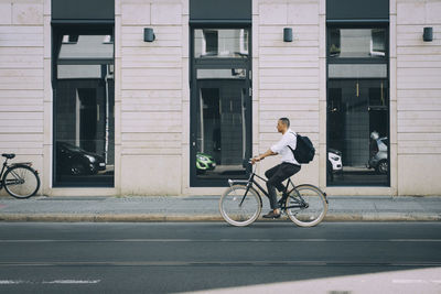 Man riding bicycle on street against building