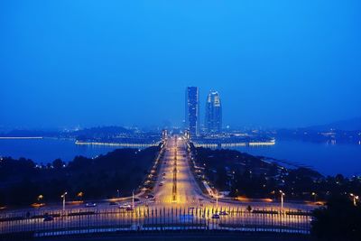 Illuminated street leading towards modern building against sky at dusk