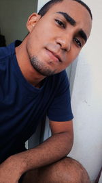 Portrait of young man sitting against wall