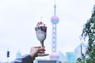 Cropped hand of woman holding ice cream in glass against sky