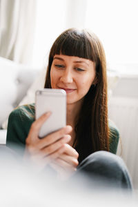 Smiling young woman using mobile phone while sitting at home