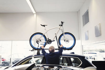 Rear view of senior man adjusting bicycle on car roof at showroom