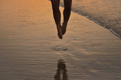 Low section of woman jumping at beach during sunset