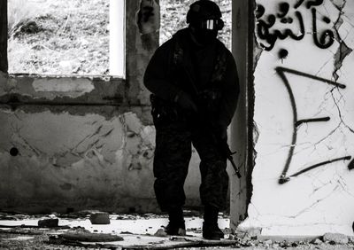 Military man with gun standing by wall