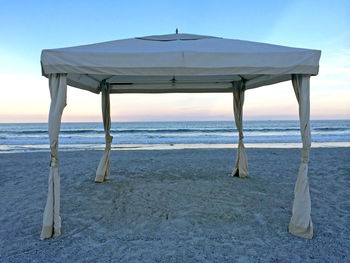 A cabana with it's sides tide back on the beach at sunset