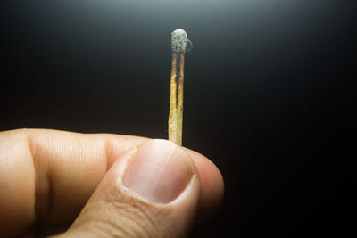 Close-up of hand holding matchstick over black background