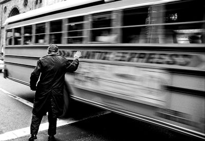 Blurred motion of bus passing by a man waving at it in black and white