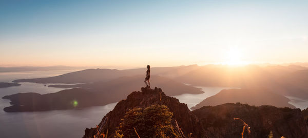 Silhouette person standing on rock against sky during sunset