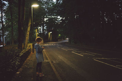 Side view of young woman using phone on road during dusk