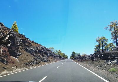 Road amidst trees against clear blue sky