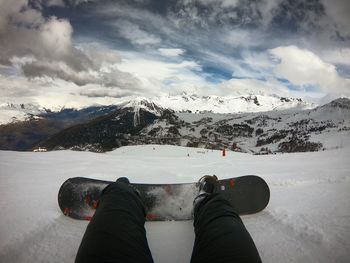 Low section of person on snowcapped mountain against sky