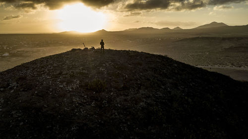 Silhouette person standing on rock against sky during sunset