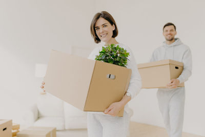 Portrait of couple carrying boxes in new house