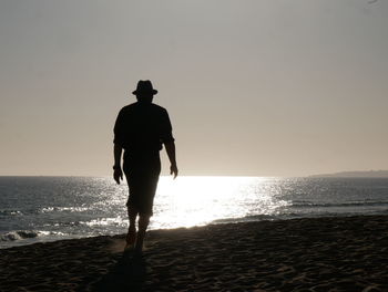 Rear view of silhouette man on beach against sky during sunset